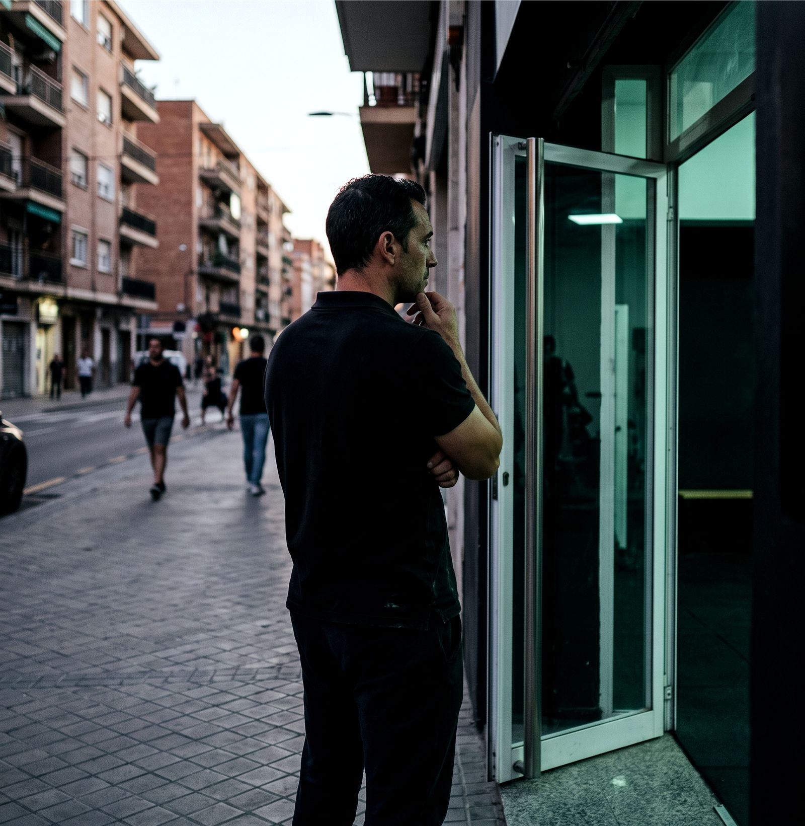 Dueño de un gimnasio de barrio en la acera, frente a su fachada, mirando la calle al caer la tarde